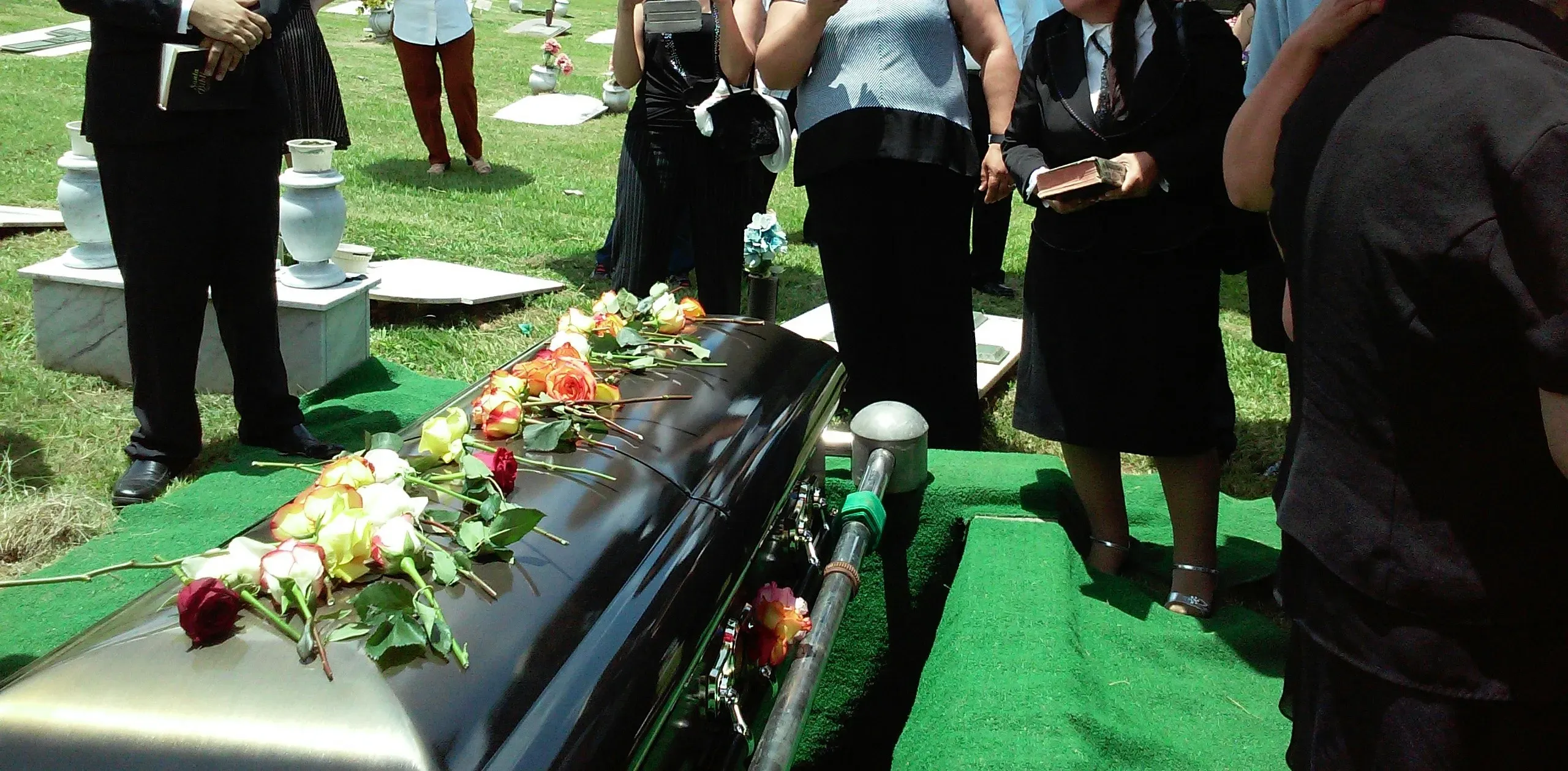 Cercueil sombre recouvert de roses lors d'une cérémonie d'inhumation au cimetière.